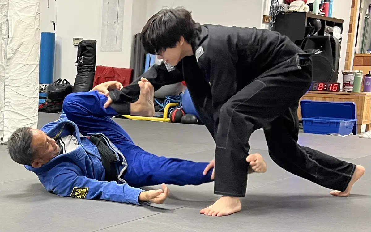 A Jiyu coach in a blue gi working guard against a student in a black gi