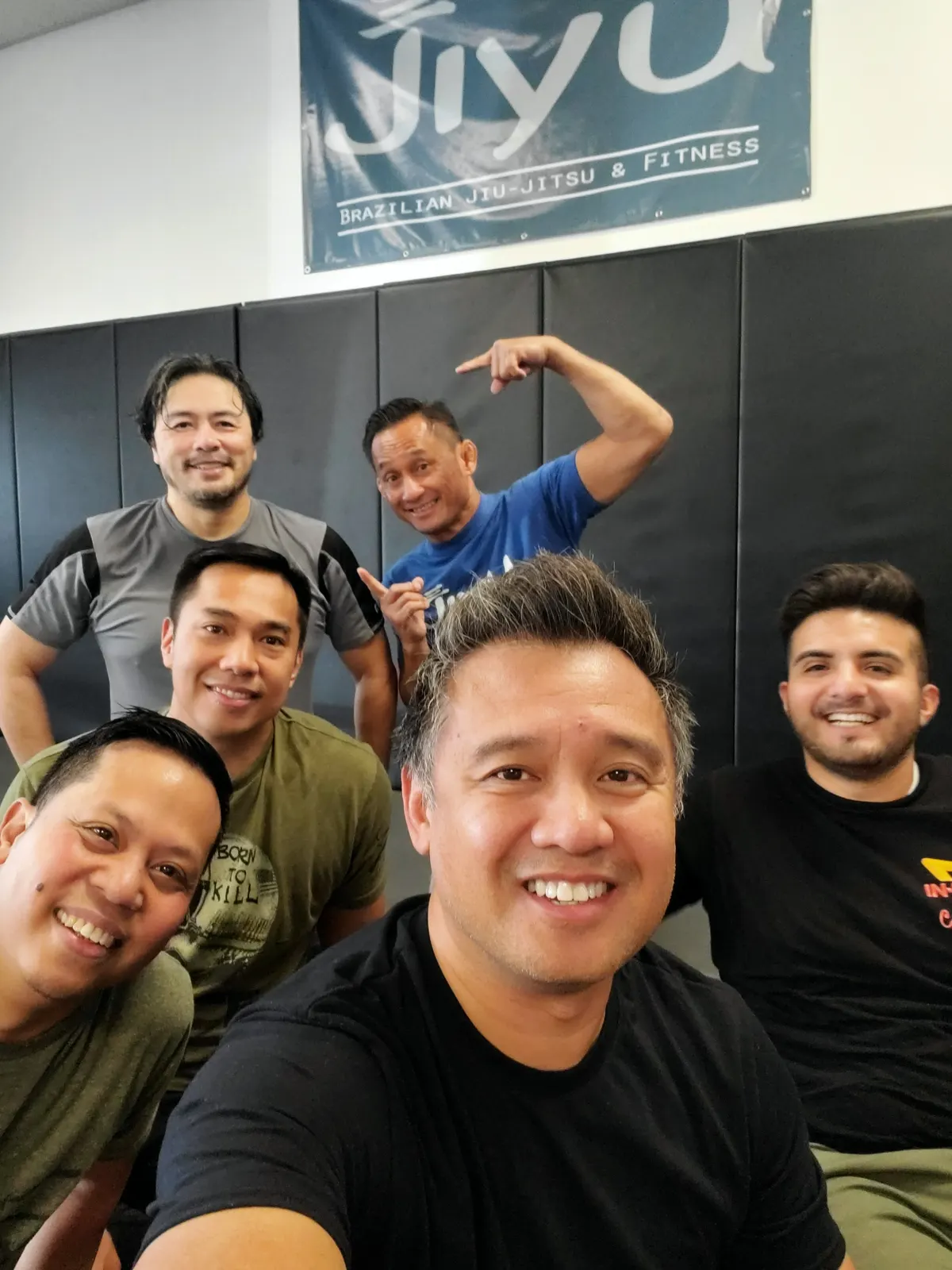 Jiyu adult students and coaches smiling together on the mats under the Jiyu banner