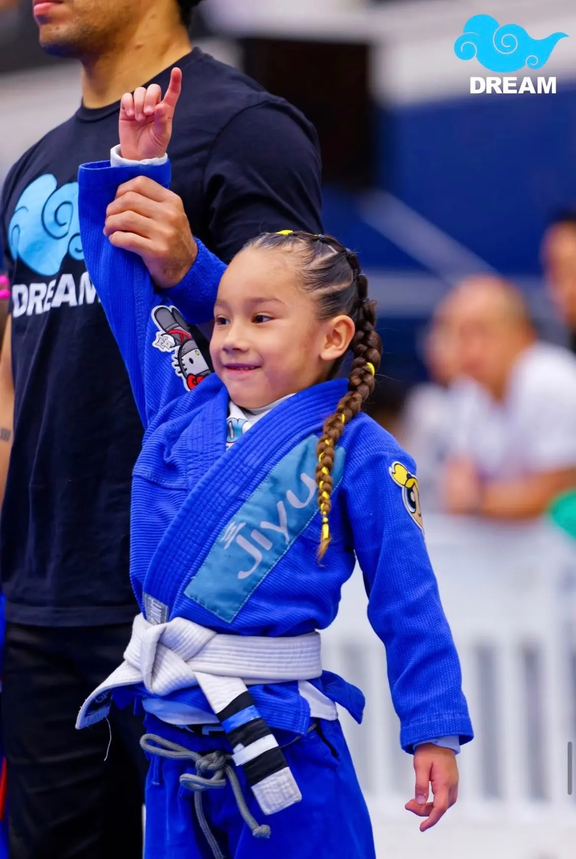 A smiling young Jiyu student in a blue gi waving at a tournament