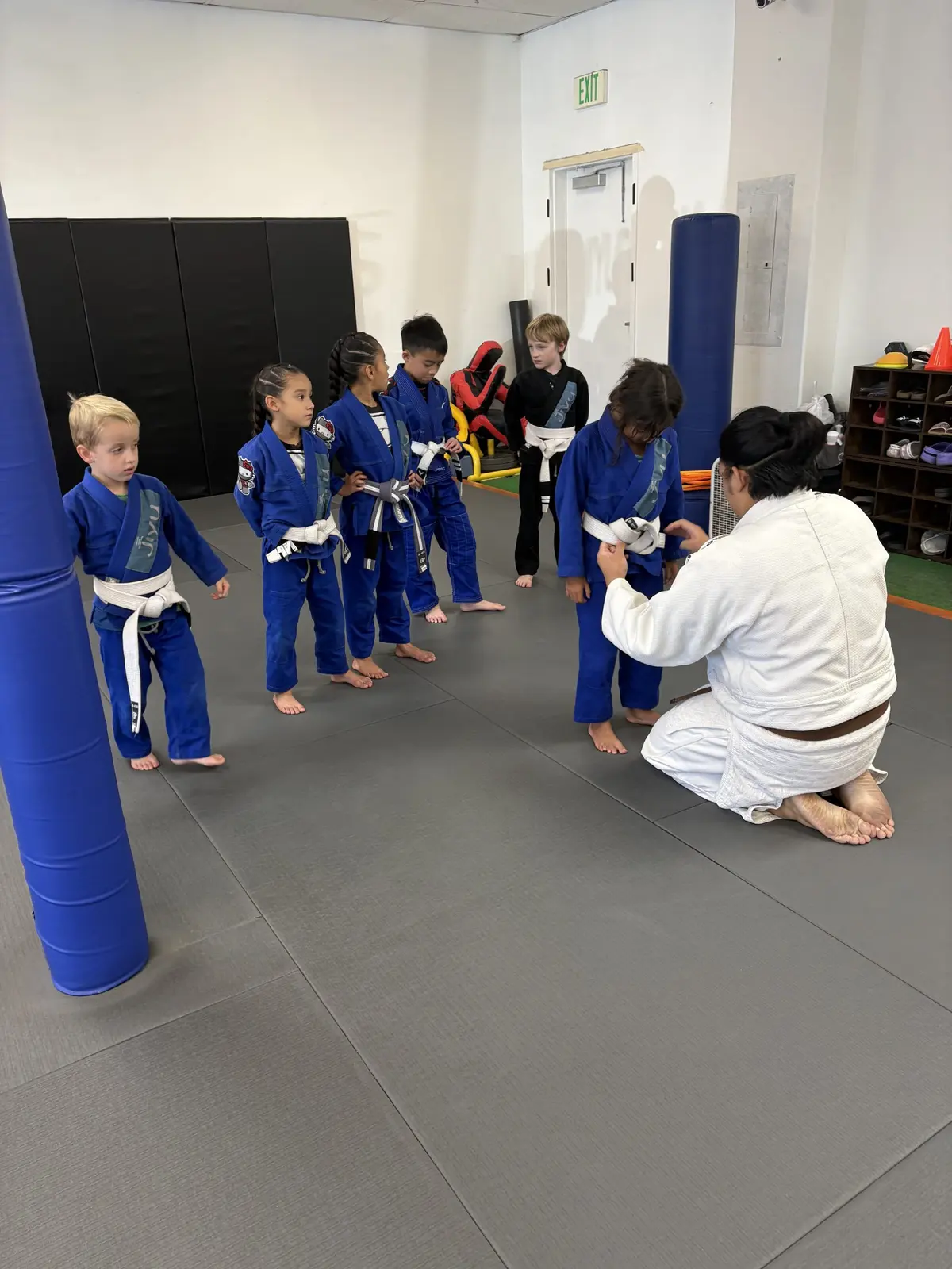 A Jiyu instructor tying a young student's belt while classmates in blue gis wait