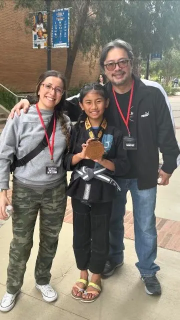 A young Jiyu student holding a gold medal with two coaches